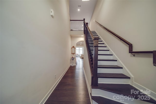 stairs with arched walkways, wood finished floors, baseboards, and a towering ceiling