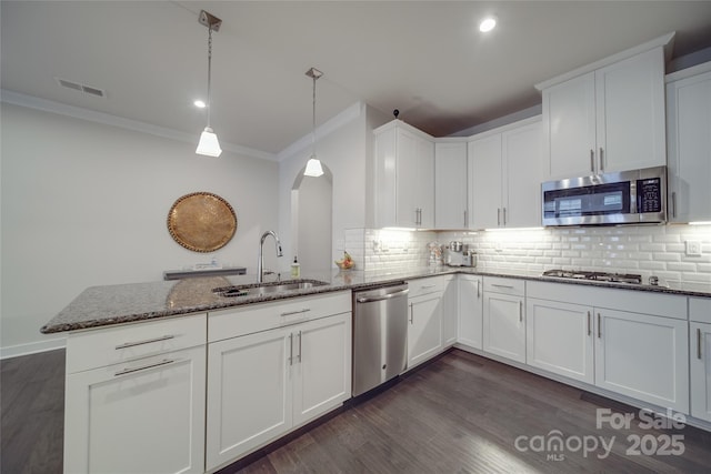 kitchen featuring stainless steel appliances, a sink, arched walkways, a peninsula, and dark stone counters
