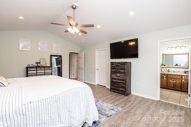 bedroom featuring a ceiling fan, light wood-style floors, baseboards, ensuite bath, and vaulted ceiling