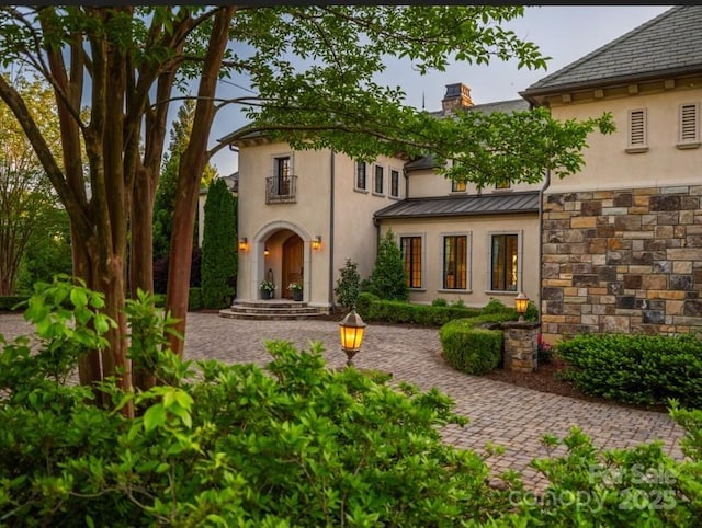 rear view of house with metal roof, stucco siding, a standing seam roof, and a chimney