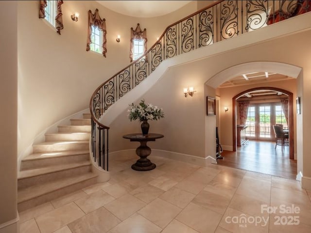 stairs with baseboards, a towering ceiling, and arched walkways