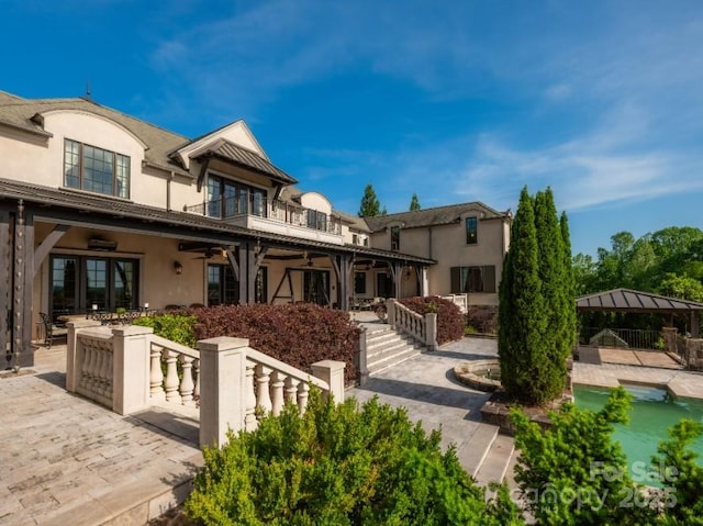 rear view of property featuring a ceiling fan, a balcony, stucco siding, and a patio