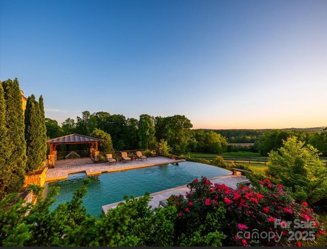 pool at dusk featuring a gazebo, a patio area, an outdoor pool, and fence