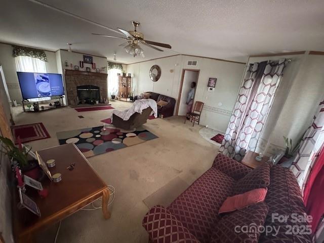 living area with ornamental molding, visible vents, ceiling fan, a brick fireplace, and carpet floors