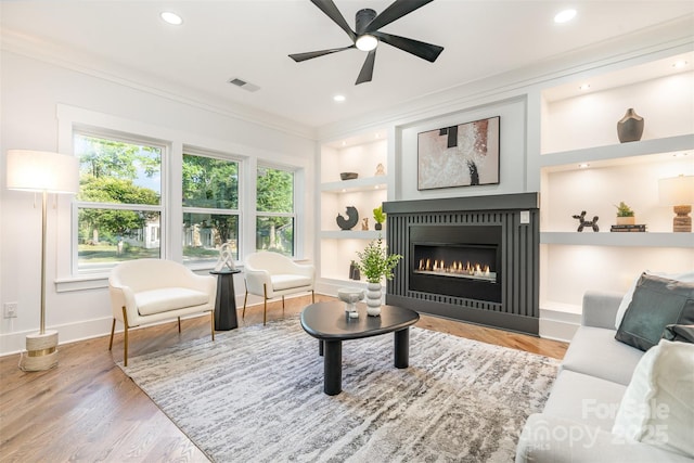 2224 Highland St, Charlotte, NC 28208 - living room featuring built in shelves, crown molding, ceiling fan, baseboards, and a glass covered fireplace