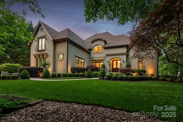 french country inspired facade with a lawn and stucco siding
