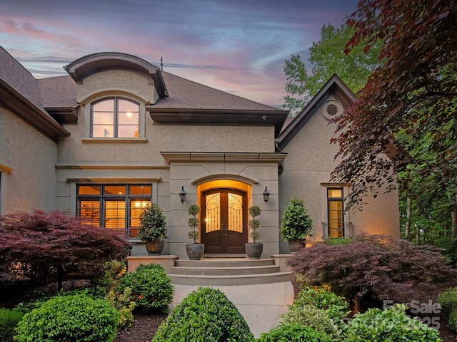 exterior entry at dusk with stucco siding and french doors