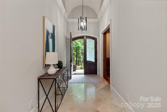 foyer entrance featuring a chandelier, ornamental molding, arched walkways, baseboards, and light tile patterned floors