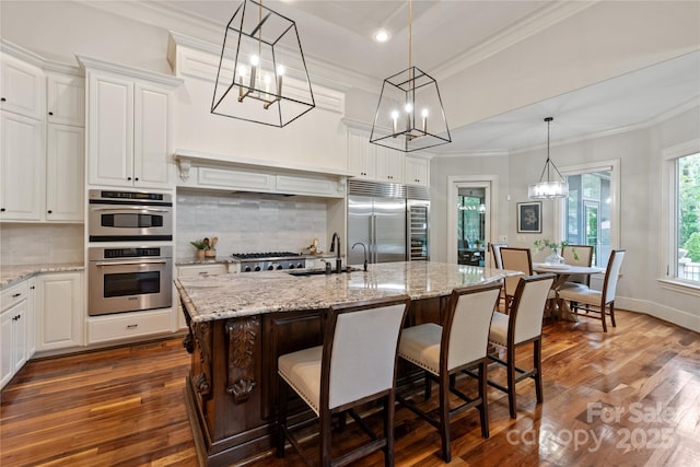 kitchen with appliances with stainless steel finishes, a chandelier, crown molding, decorative backsplash, and a sink