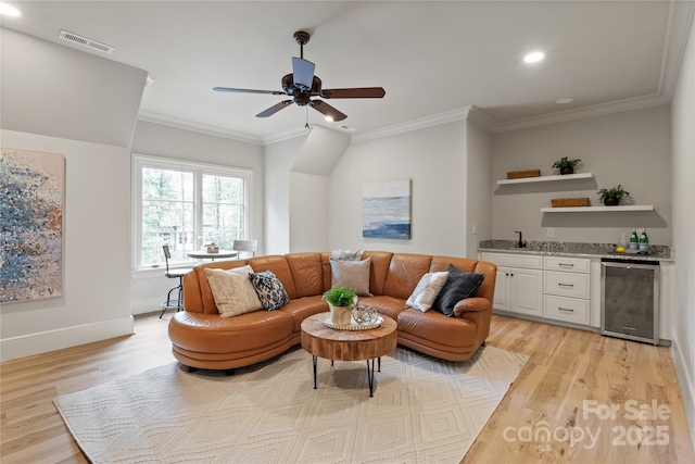 living area featuring beverage cooler, bar with sink, light wood-style flooring, ornamental molding, and recessed lighting