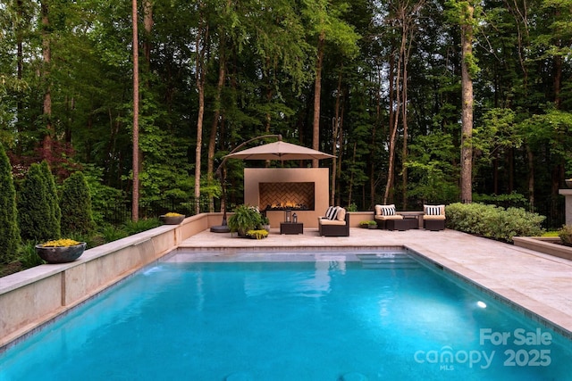 outdoor pool featuring an outdoor hangout area, a patio area, and a wooded view