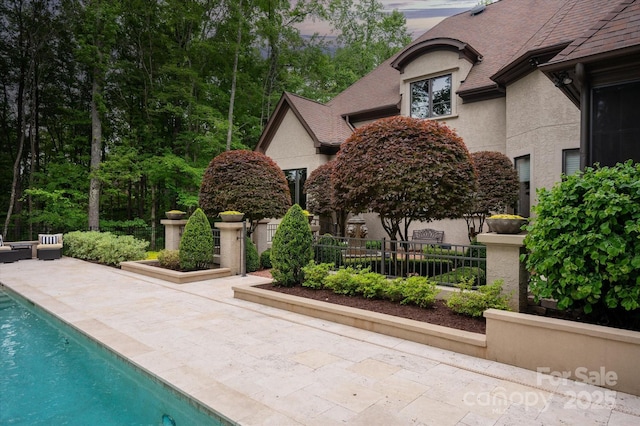 view of side of home featuring stucco siding, a patio area, an outdoor pool, fence, and a shingled roof