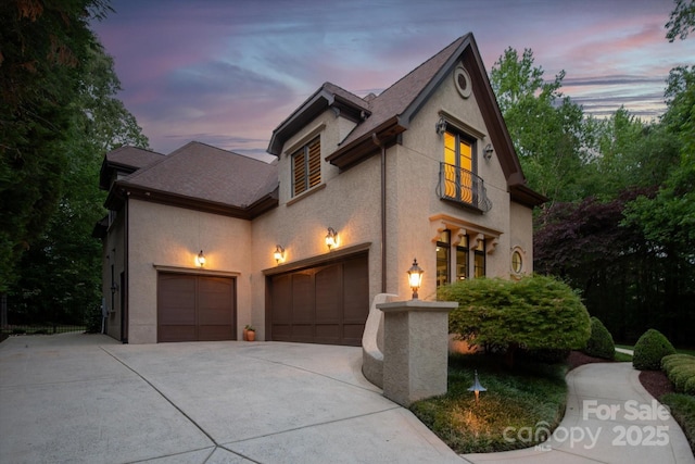 french country home with concrete driveway, an attached garage, and stucco siding