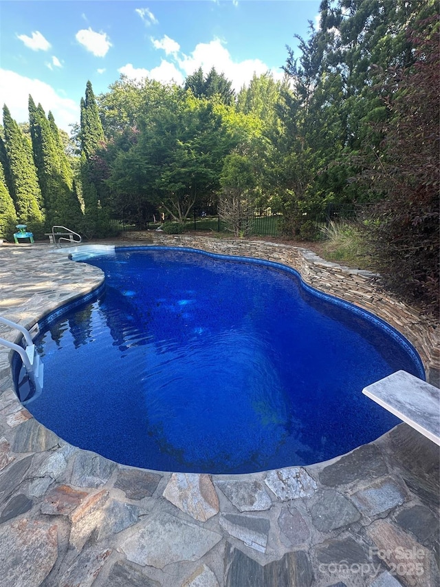 swimming pool featuring a patio area, fence, and a diving board