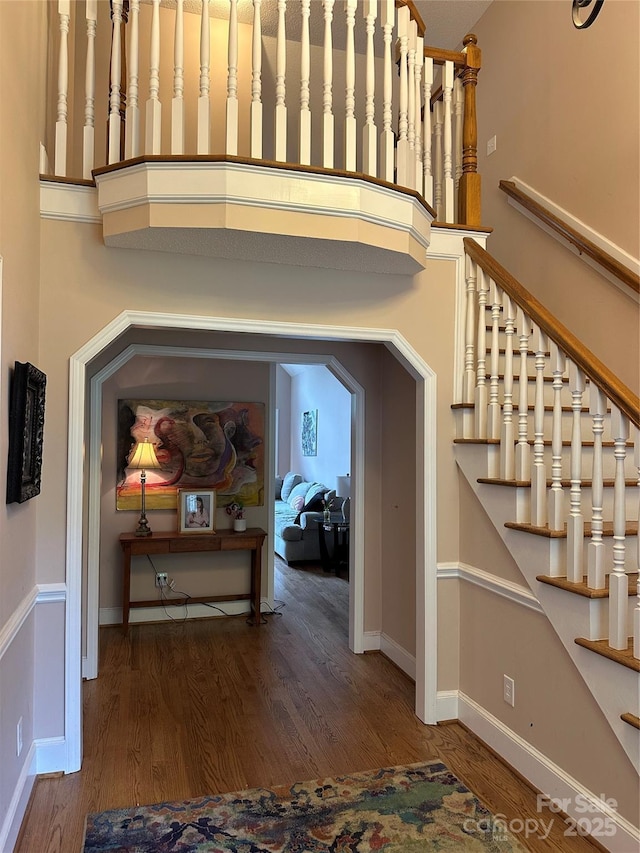 stairway with wood finished floors, baseboards, and a towering ceiling