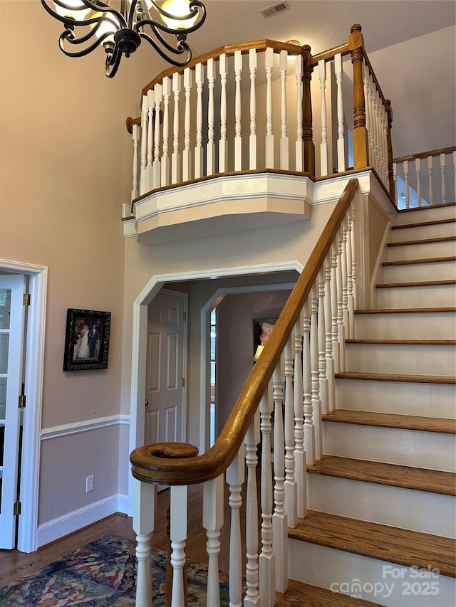 staircase featuring a chandelier, baseboards, wood finished floors, and a towering ceiling