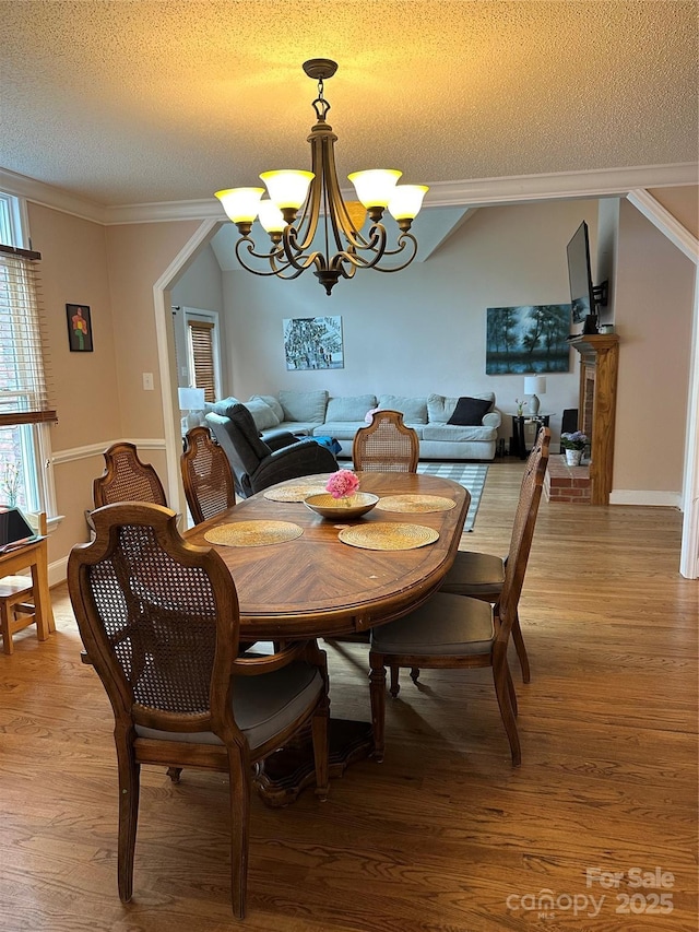 dining room with a textured ceiling, a chandelier, light wood-style flooring, and ornamental molding
