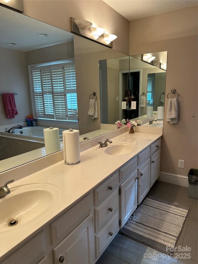 bathroom with a textured ceiling, double vanity, tile patterned flooring, baseboards, and a tub