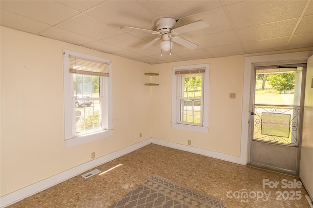unfurnished room featuring a wealth of natural light, visible vents, baseboards, and ceiling fan