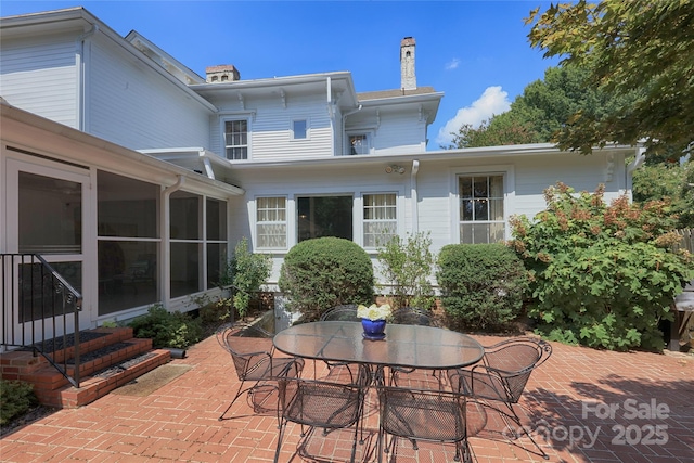 rear view of house with a patio, outdoor dining space, a sunroom, a chimney, and entry steps
