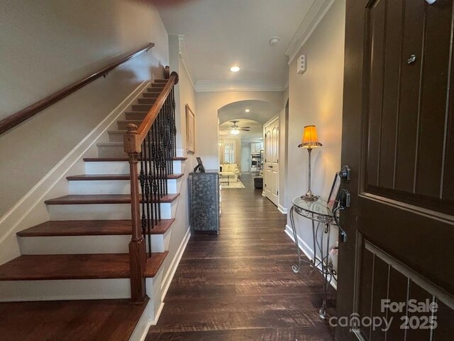 stairway featuring ornamental molding, wood finished floors, arched walkways, a ceiling fan, and baseboards