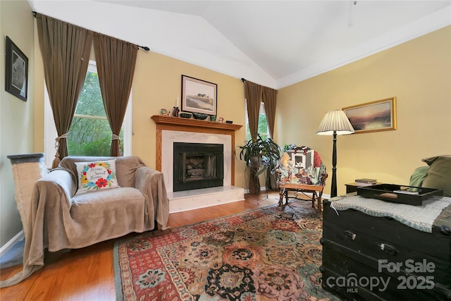 sitting room featuring lofted ceiling, wood finished floors, a fireplace with raised hearth, and baseboards