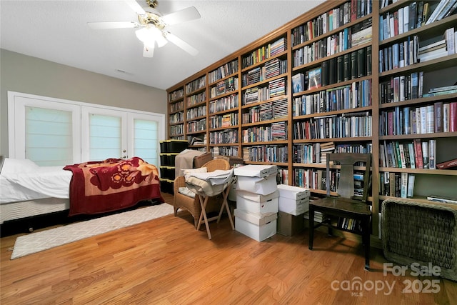 living area with wood finished floors, wall of books, and ceiling fan