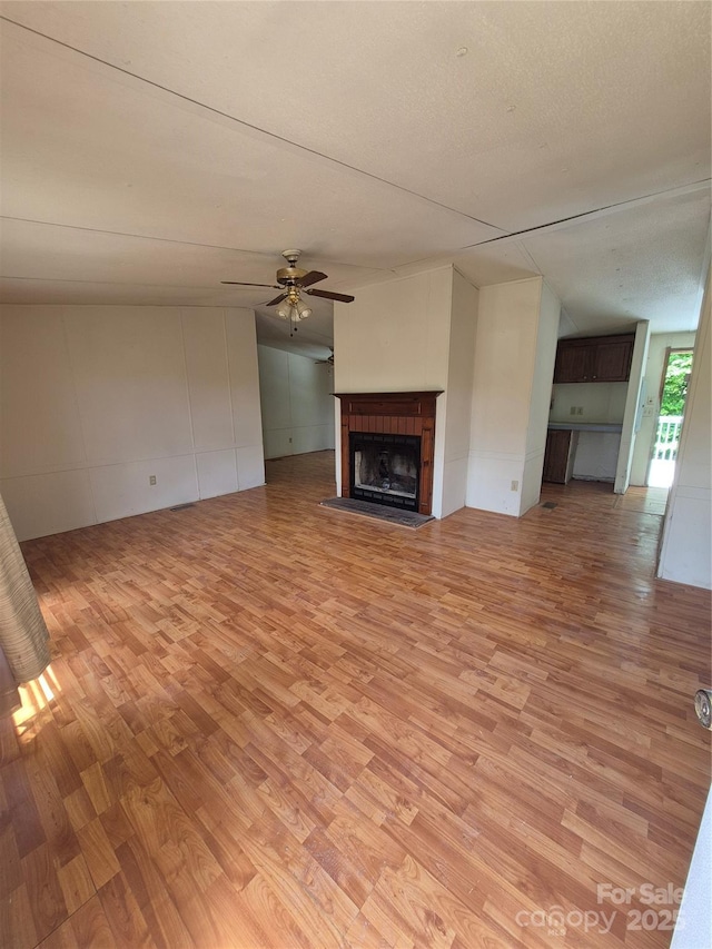 unfurnished living room featuring a ceiling fan, light wood finished floors, and a fireplace with raised hearth
