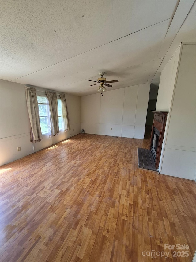 unfurnished living room with a ceiling fan, a brick fireplace, and light wood finished floors