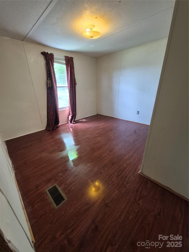 unfurnished room with a textured ceiling, visible vents, and wood finished floors