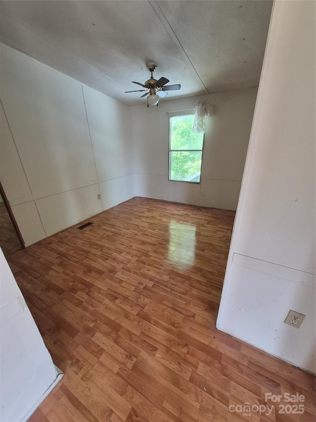 unfurnished room with ceiling fan, a textured ceiling, visible vents, and wood finished floors