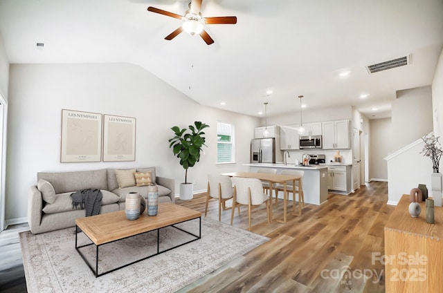 living room with lofted ceiling, light wood-style flooring, baseboards, ceiling fan, and visible vents