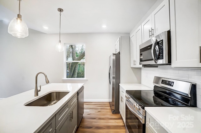 kitchen with hanging light fixtures, a sink, backsplash, light countertops, and appliances with stainless steel finishes