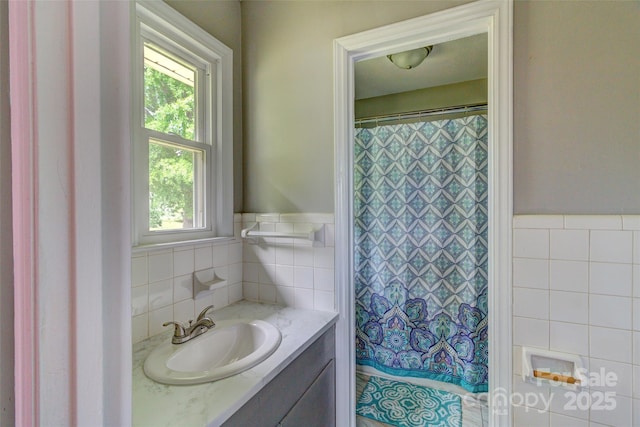 full bath featuring vanity, tile walls, a wainscoted wall, and plenty of natural light