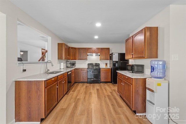 kitchen featuring black appliances, a sink, light wood-type flooring, under cabinet range hood, and brown cabinets