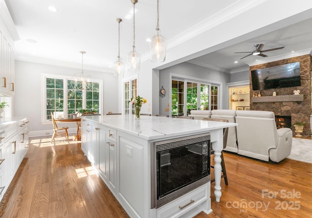 12835 Ninebark Trl, Charlotte, NC 28278 - kitchen with black microwave, a fireplace, ornamental molding, wood finished floors, and white cabinetry
