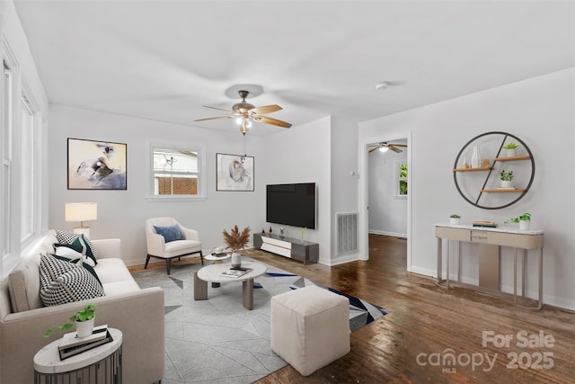 living area featuring baseboards, visible vents, ceiling fan, and wood finished floors