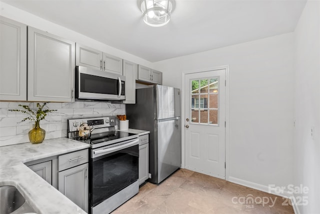 kitchen featuring gray cabinets, baseboards, backsplash, appliances with stainless steel finishes, and marble finish floor