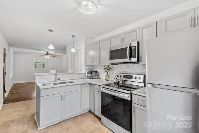 kitchen featuring a ceiling fan, a sink, a peninsula, backsplash, and appliances with stainless steel finishes