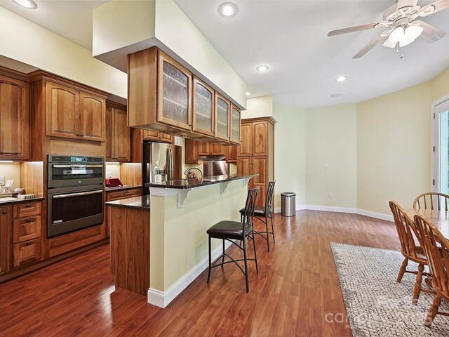 1140 Fern Hill Rd, Mooresville, NC 28117 - kitchen with stainless steel fridge with ice dispenser, a breakfast bar, multiple ovens, glass insert cabinets, and dark wood-style floors