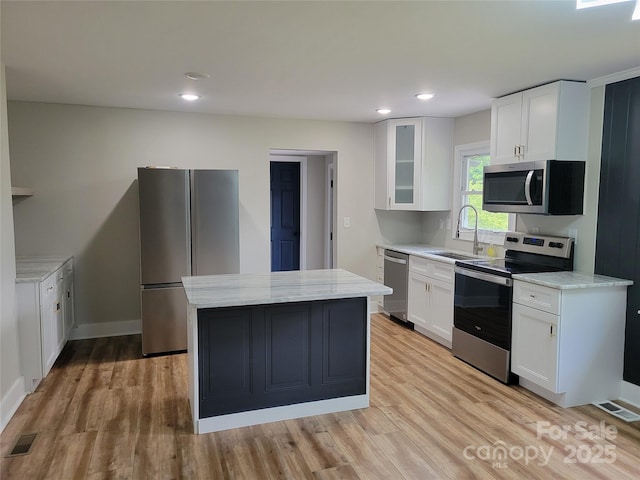 kitchen with stainless steel appliances, a sink, a center island, light wood finished floors, and recessed lighting
