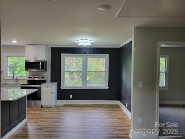kitchen featuring appliances with stainless steel finishes, a sink, white cabinets, light countertops, and ornamental molding