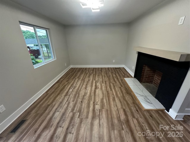 unfurnished living room featuring a fireplace with flush hearth, dark wood finished floors, and baseboards