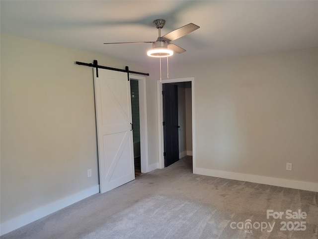 unfurnished bedroom featuring a barn door, carpet, baseboards, and a ceiling fan