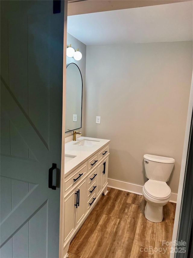 bathroom featuring wood finished floors, toilet, baseboards, and double vanity