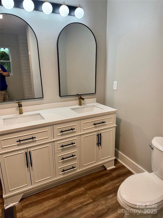 bathroom with wood finished floors, toilet, double vanity, and baseboards