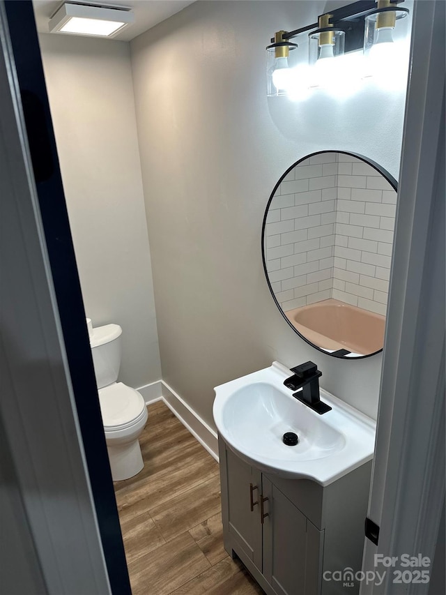 half bathroom featuring vanity, toilet, wood finished floors, and baseboards