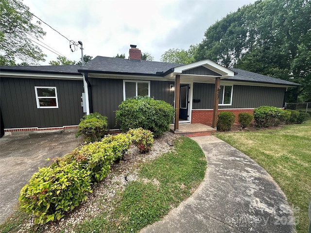 view of front of home with a chimney, a front yard, brick siding, and roof with shingles