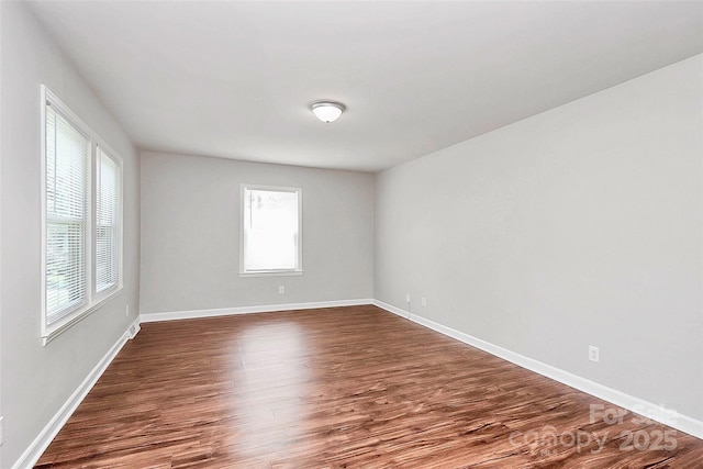 empty room featuring dark wood finished floors, plenty of natural light, and baseboards