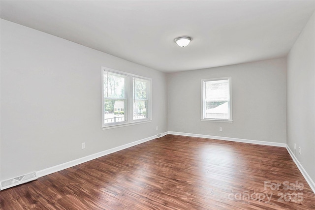 unfurnished room with visible vents, a healthy amount of sunlight, and dark wood-style floors